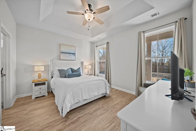 bedroom with light wood-type flooring, ceiling fan, and a tray ceiling