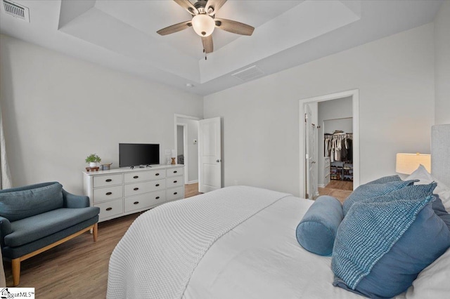 bedroom featuring ceiling fan, hardwood / wood-style floors, a raised ceiling, a walk in closet, and a closet