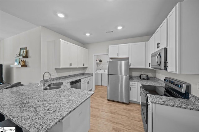 kitchen featuring washer and dryer, kitchen peninsula, sink, white cabinetry, and stainless steel appliances