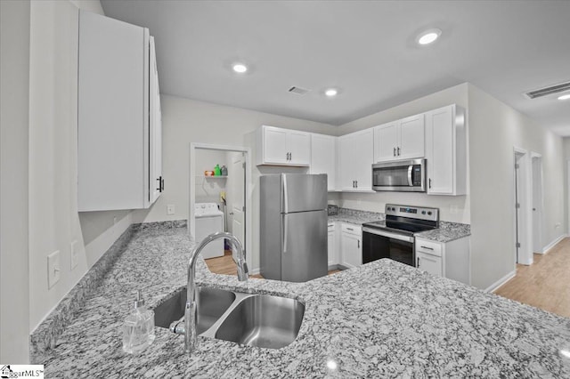 kitchen with white cabinets, appliances with stainless steel finishes, sink, light wood-type flooring, and light stone counters