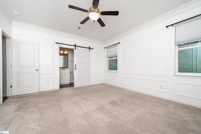 unfurnished bedroom with connected bathroom, ornamental molding, carpet flooring, ceiling fan, and a barn door