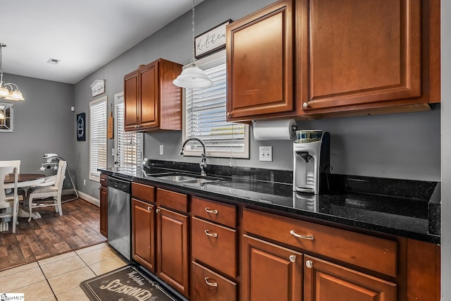 kitchen with dark stone countertops, stainless steel dishwasher, sink, hanging light fixtures, and light tile patterned floors