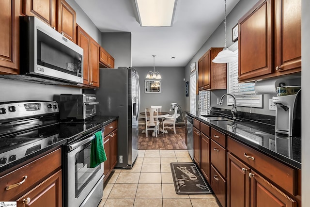 kitchen featuring appliances with stainless steel finishes, light tile patterned flooring, dark stone counters, pendant lighting, and sink