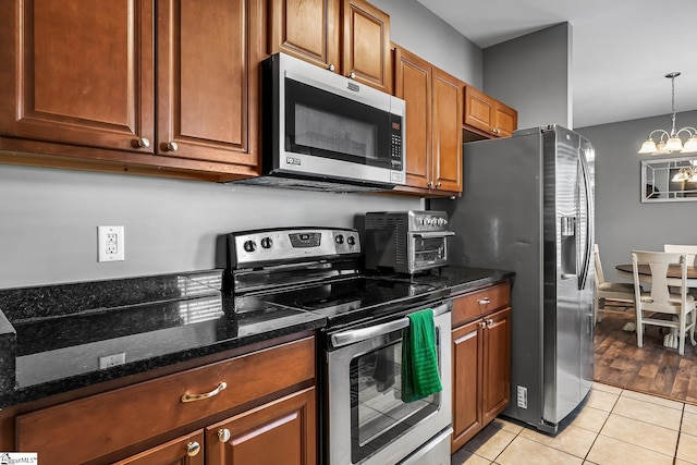 kitchen featuring dark stone countertops, pendant lighting, stainless steel appliances, light tile patterned floors, and a chandelier