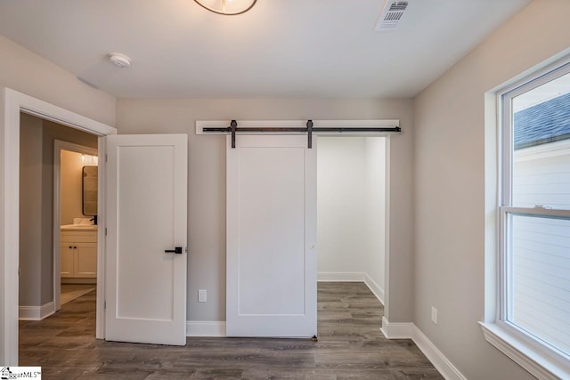 unfurnished bedroom featuring dark wood-type flooring, multiple windows, a barn door, and ensuite bath