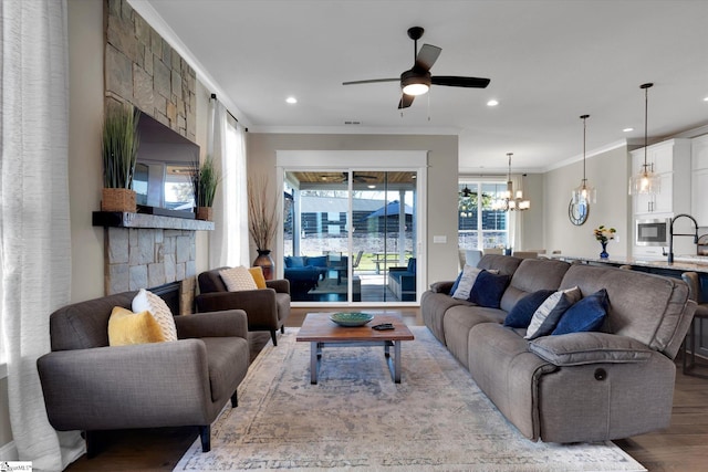 living room featuring ceiling fan with notable chandelier, a fireplace, light hardwood / wood-style floors, sink, and ornamental molding