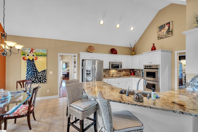 kitchen with white cabinetry, stainless steel appliances, decorative backsplash, sink, and hanging light fixtures