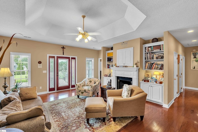 living room with dark wood-type flooring, ceiling fan, a textured ceiling, and a tray ceiling