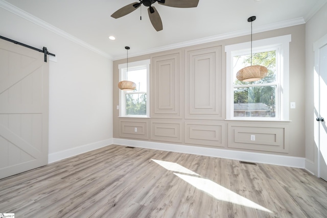 spare room featuring a barn door, baseboards, visible vents, light wood-style flooring, and crown molding