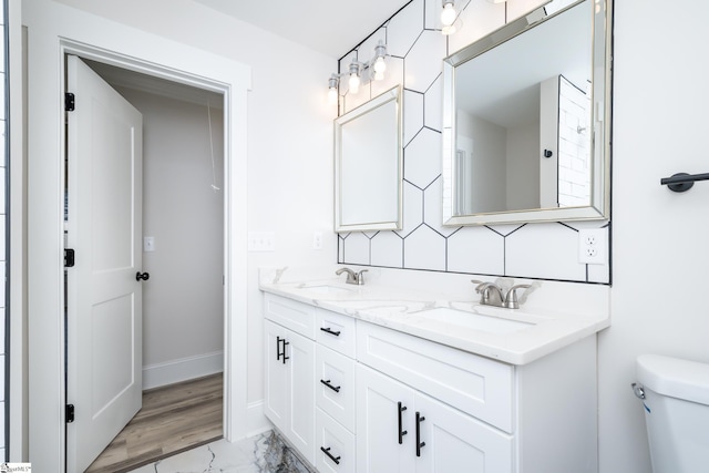 bathroom featuring baseboards, a sink, toilet, and double vanity