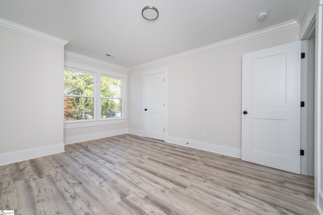 empty room with baseboards, crown molding, and light wood finished floors