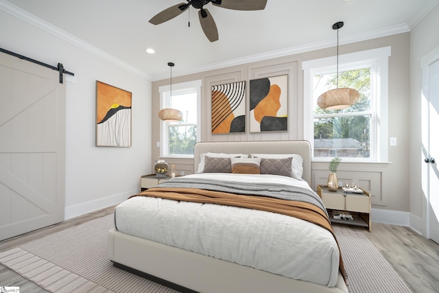 bedroom with ornamental molding, a barn door, multiple windows, and light wood-style flooring