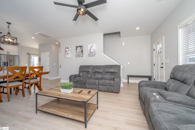 living room with light hardwood / wood-style floors and ceiling fan with notable chandelier