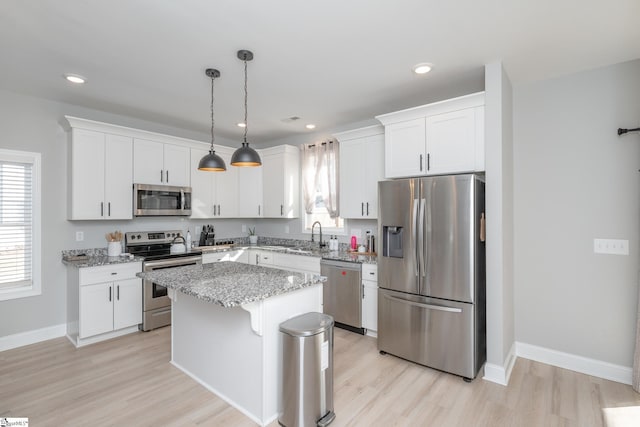 kitchen featuring appliances with stainless steel finishes, white cabinets, hanging light fixtures, a kitchen island, and light stone counters