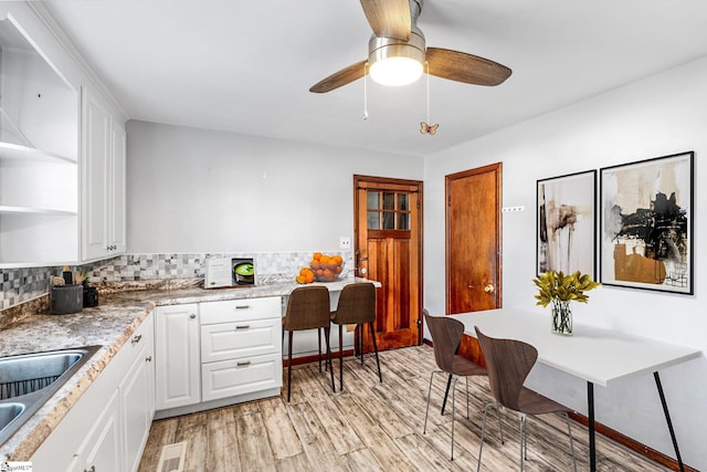 kitchen with ceiling fan, decorative backsplash, white cabinets, light hardwood / wood-style flooring, and sink