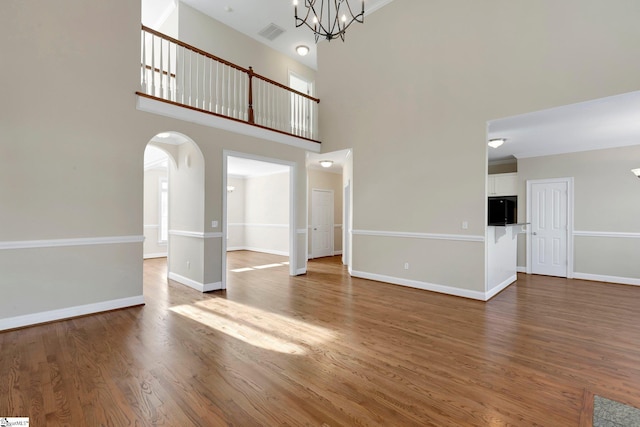 unfurnished living room with wood-type flooring, a towering ceiling, and a notable chandelier