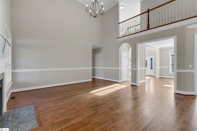 unfurnished living room with dark wood-type flooring, a chandelier, a towering ceiling, and a tiled fireplace