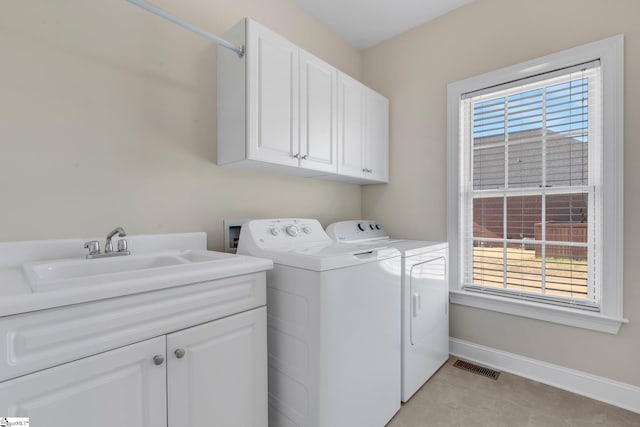 clothes washing area featuring a healthy amount of sunlight, washing machine and dryer, sink, and cabinets