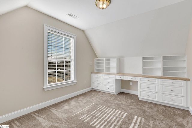 unfurnished office with built in desk, lofted ceiling, and light colored carpet