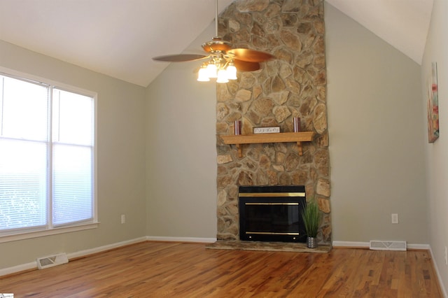 unfurnished living room with lofted ceiling, a wealth of natural light, a stone fireplace, and hardwood / wood-style flooring