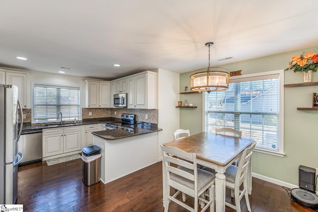 kitchen with appliances with stainless steel finishes, sink, white cabinetry, and decorative light fixtures