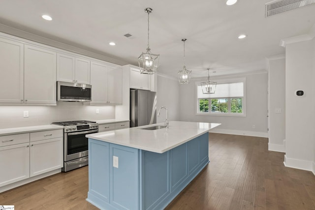 kitchen featuring hanging light fixtures, white cabinets, a kitchen island with sink, and appliances with stainless steel finishes