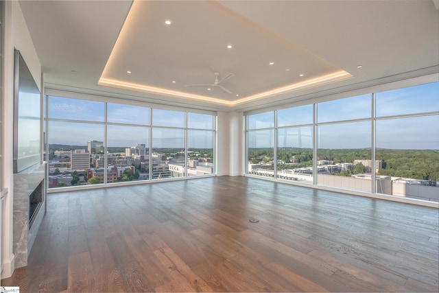 empty room featuring ceiling fan, a wall of windows, wood-type flooring, and a tray ceiling