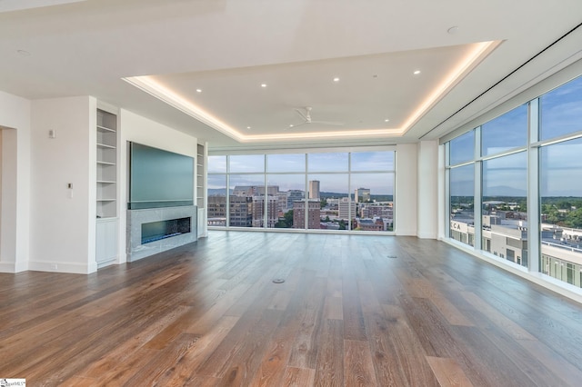 unfurnished living room with built in shelves, a tray ceiling, a wealth of natural light, and hardwood / wood-style floors