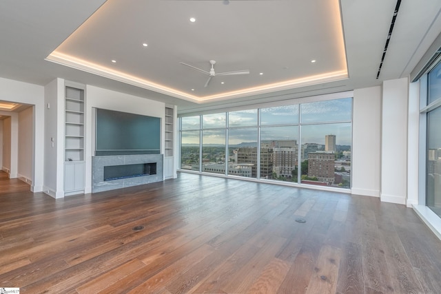 unfurnished living room with ceiling fan, built in shelves, and a tray ceiling