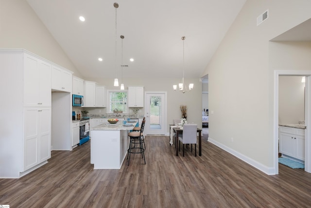 kitchen with a kitchen island, stainless steel stove, white cabinets, and decorative light fixtures