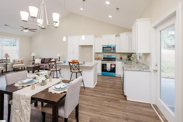 dining space with high vaulted ceiling, ceiling fan with notable chandelier, and hardwood / wood-style floors