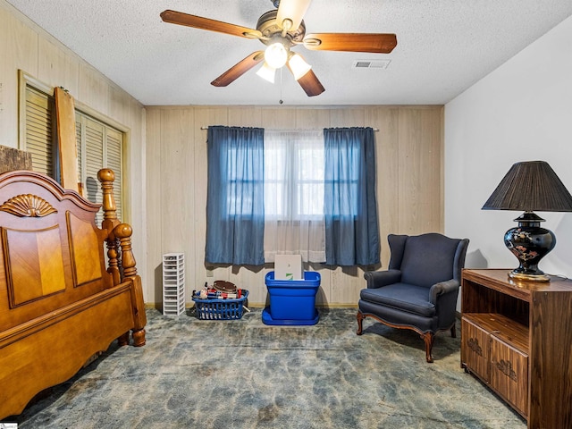 sitting room with dark colored carpet, ceiling fan, a textured ceiling, and wooden walls