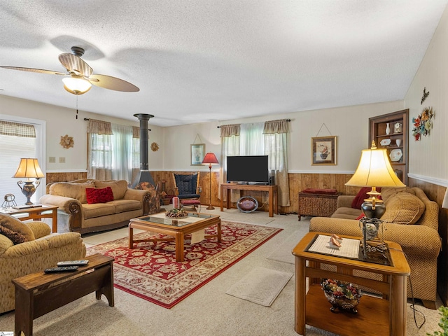 living room with ceiling fan, a wood stove, a textured ceiling, and wood walls