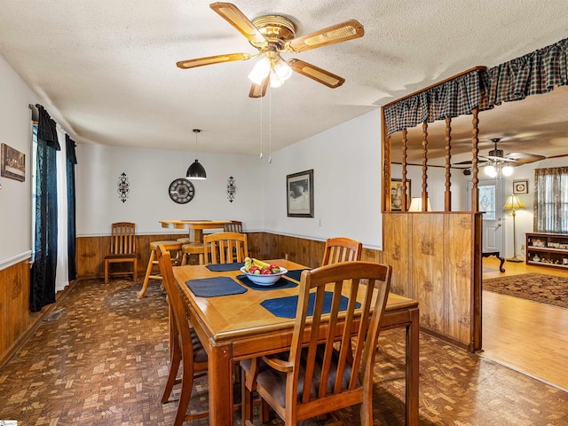 dining room featuring ceiling fan, wooden walls, parquet floors, and a textured ceiling