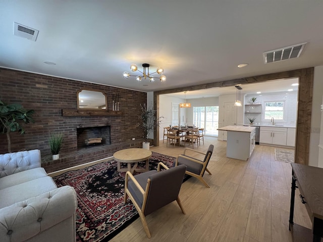 living room featuring a brick fireplace, light hardwood / wood-style floors, sink, an inviting chandelier, and brick wall