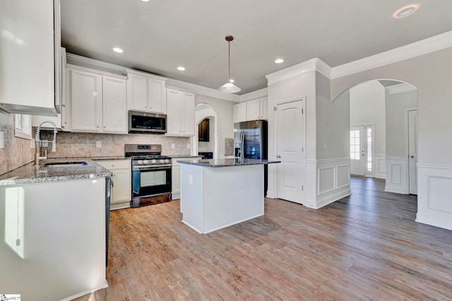 kitchen with sink, appliances with stainless steel finishes, a kitchen island, decorative backsplash, and white cabinets