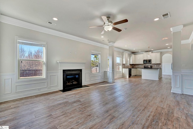 unfurnished living room featuring crown molding, light hardwood / wood-style flooring, ceiling fan, a premium fireplace, and decorative columns