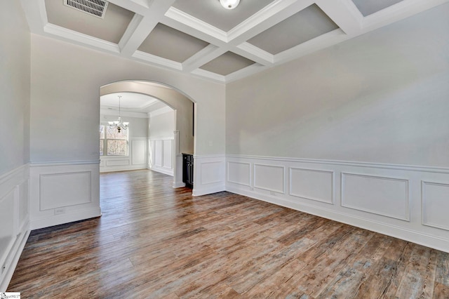 empty room featuring crown molding, an inviting chandelier, beam ceiling, coffered ceiling, and wood-type flooring