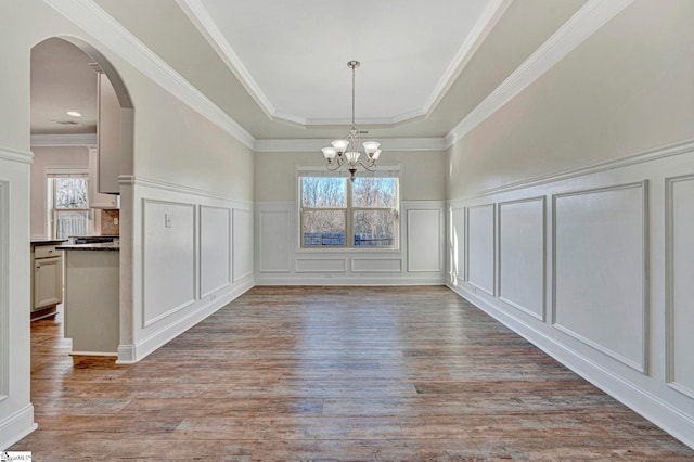 unfurnished dining area featuring an inviting chandelier, crown molding, a raised ceiling, and light wood-type flooring