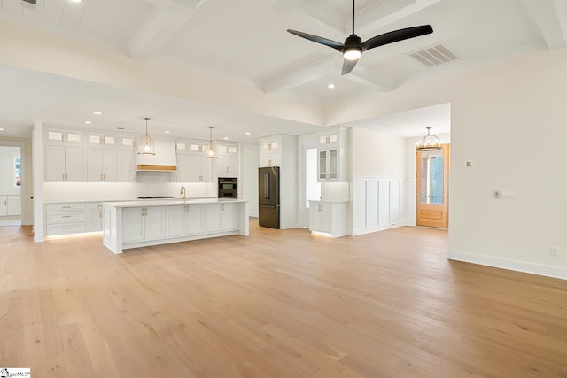 unfurnished living room featuring ceiling fan with notable chandelier, sink, beamed ceiling, and light wood-type flooring