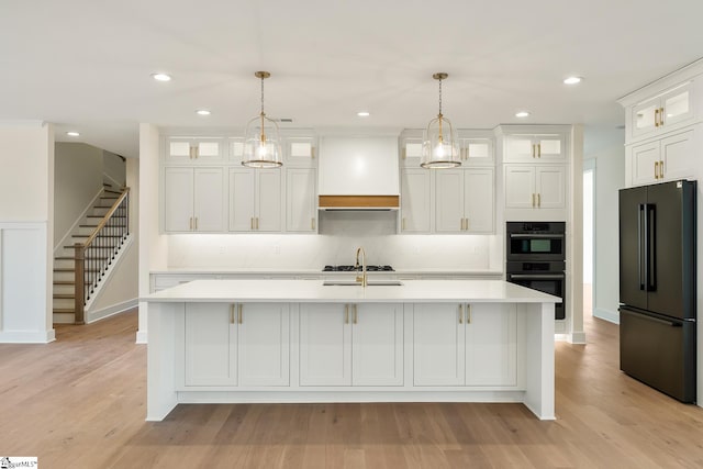 kitchen with decorative light fixtures, white cabinetry, black appliances, and an island with sink