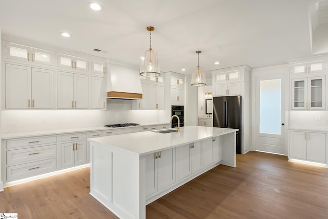 kitchen with stainless steel gas stovetop, premium range hood, white cabinetry, an island with sink, and sink