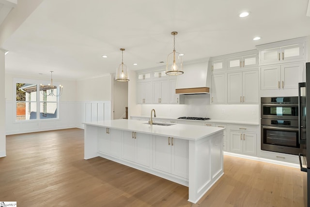 kitchen with gas cooktop, sink, white cabinetry, and a center island with sink