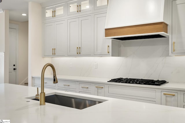 kitchen with white cabinetry, custom exhaust hood, tasteful backsplash, black gas stovetop, and sink