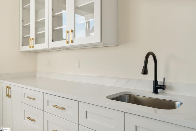 kitchen with light stone countertops, white cabinetry, and sink