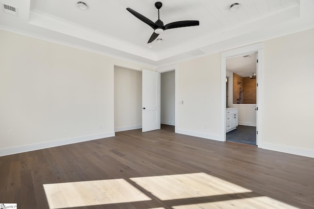 unfurnished bedroom with ensuite bath, ceiling fan, dark hardwood / wood-style floors, and a raised ceiling