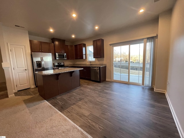 kitchen featuring dark hardwood / wood-style floors, a center island, sink, appliances with stainless steel finishes, and a breakfast bar area