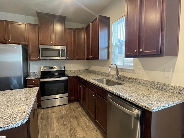 kitchen with light stone countertops, sink, appliances with stainless steel finishes, and light hardwood / wood-style flooring