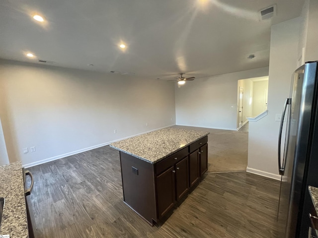 kitchen with light stone countertops, dark hardwood / wood-style floors, a kitchen island, and stainless steel refrigerator