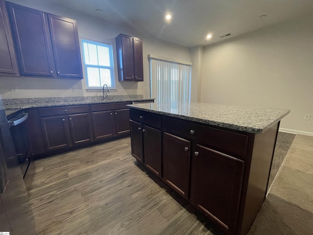 kitchen featuring a center island, sink, light stone counters, and hardwood / wood-style floors